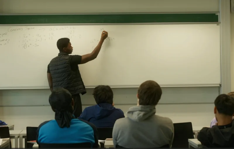 A tutor working through completing the square at the whiteboard, in front of the Saturday class at UCC